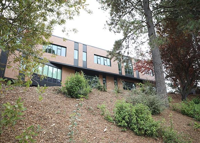 looking up a hill with trees and shrubs to a brown two story building